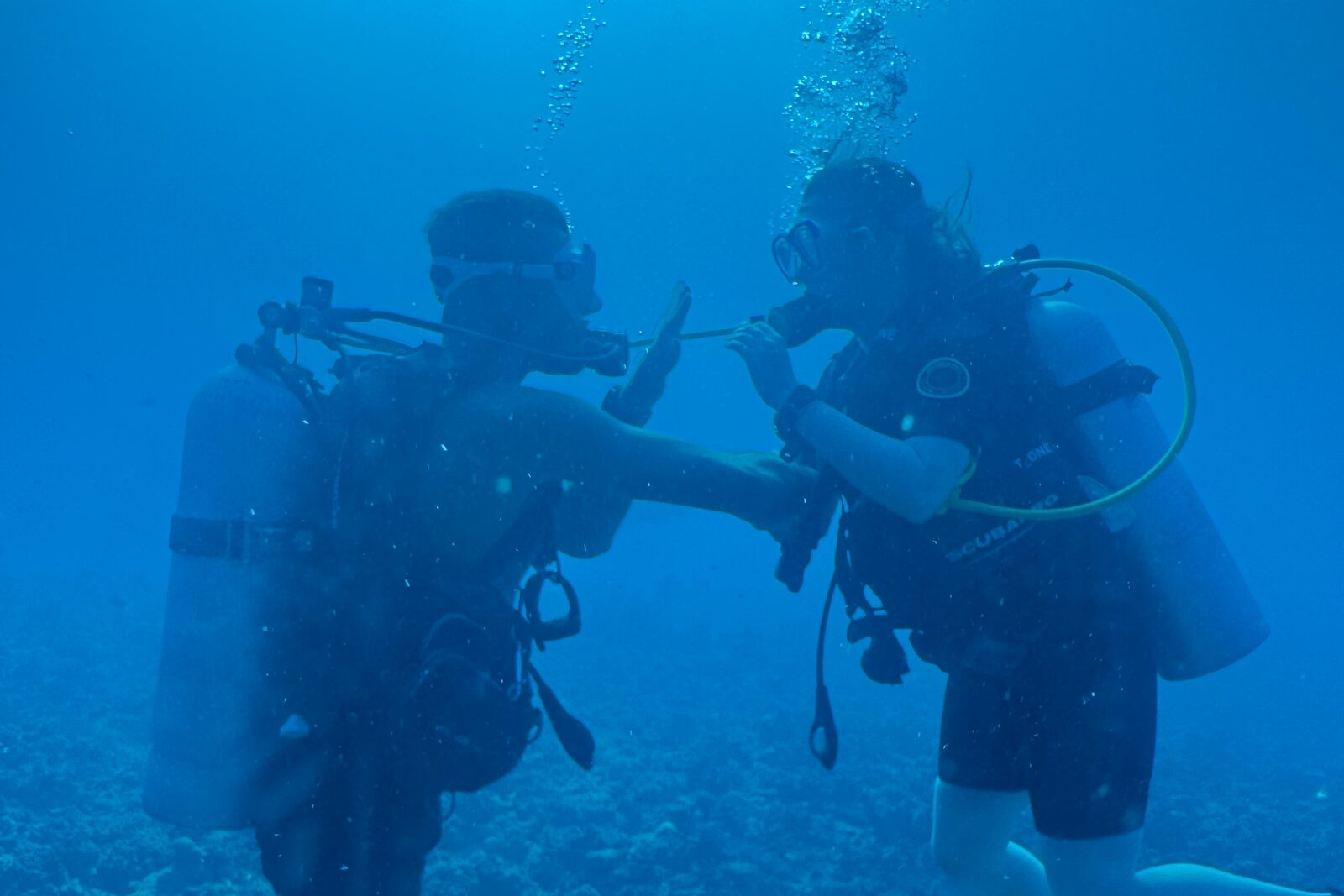 An instructor and a student practising with the regulator, in the ocean